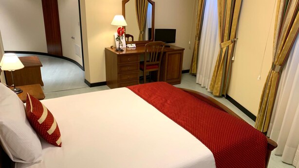 A hotel room with a large bed, a desk with a mirror, a chair, a lamp, and a TV. - Albergo Italia (Fossalta di Piave)