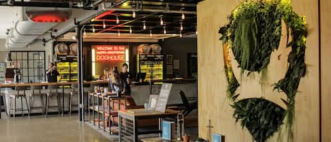A modern hotel lobby with a reception desk, bar area, and a large wall-mounted plant.