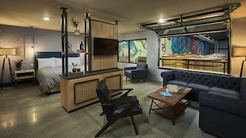 A modern living room with a sofa, a coffee table, a chair, a bed, a TV, and a kitchen area.