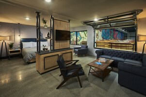 Una sala de estar moderna con sofá, mesa de centro, sillón, cama, televisor y zona de cocina.