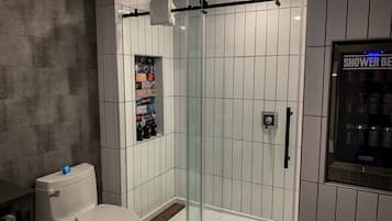 A modern bathroom with a glass shower enclosure, a toilet, and a wall-mounted shelf with various items.