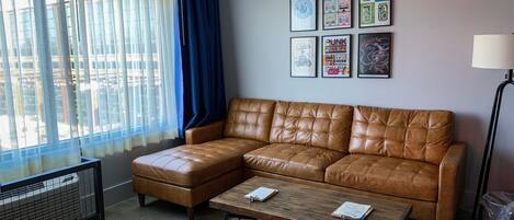 A living room with a brown leather sofa, a wooden coffee table, and a window with sheer curtains.