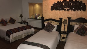 Une chambre d’hôtel avec deux lits, chacun agrémenté d’une couvre-lit à motifs et de plusieurs oreillers. On y trouve une table de chevet avec une lampe, ainsi qu’une petite table sur laquelle est posé un objet décoratif. La chambre a une atmosphère chaleureuse et accueillante, et un élément décoratif orne le mur au-dessus des lits.