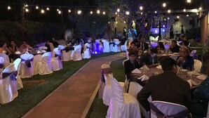 Un espace de restauration en plein air, avec des tables et des chaises disposées le long d’un sentier, entouré d’arbres et illuminé de guirlandes lumineuses.