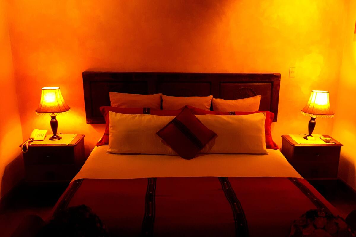 Una habitación de hotel con una cama grande, dos mesitas de noche con lámparas y un cabecero.