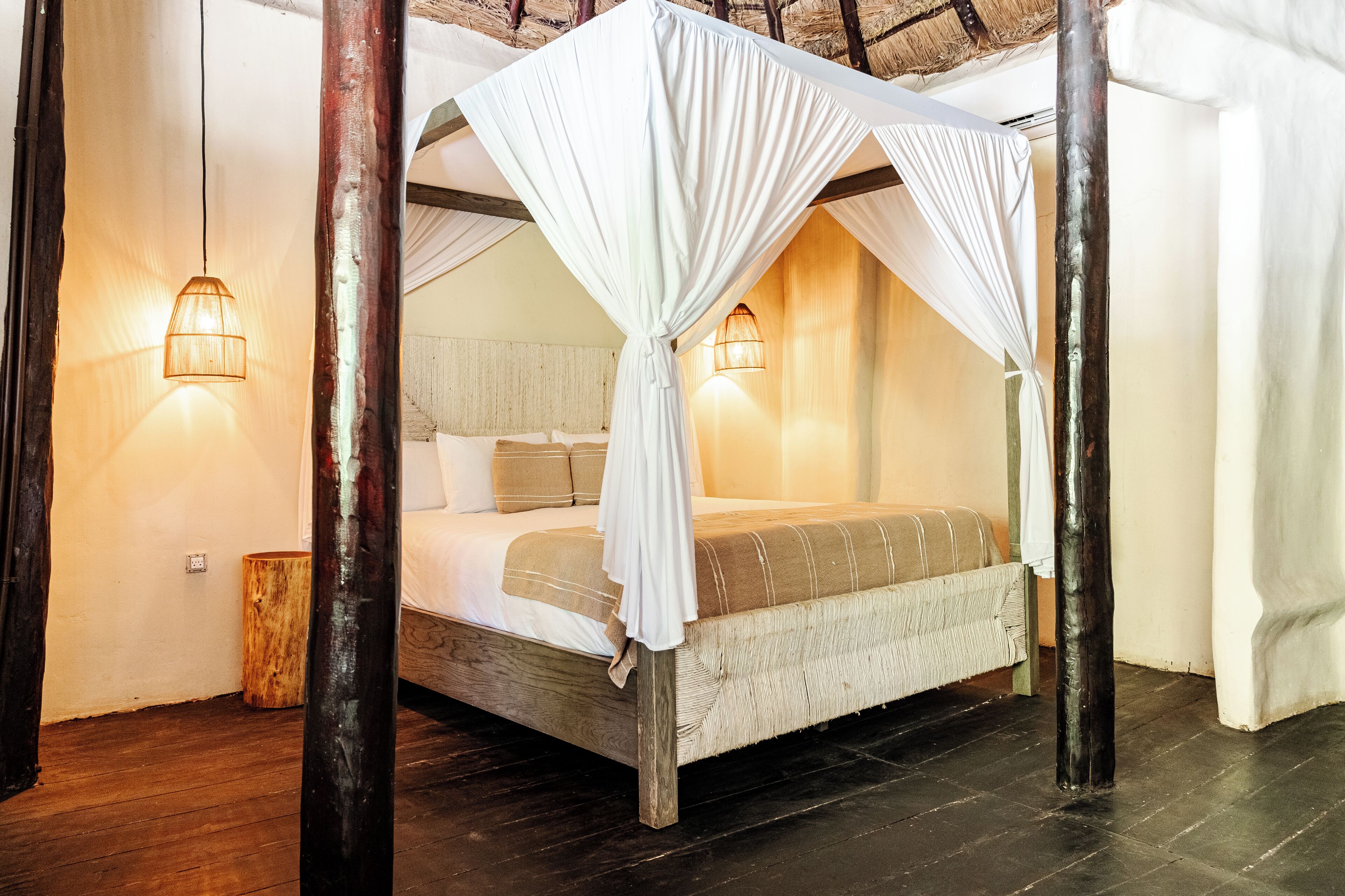 A four-poster canopy bed with white drapes, wooden posts, and two wall-mounted lamps.