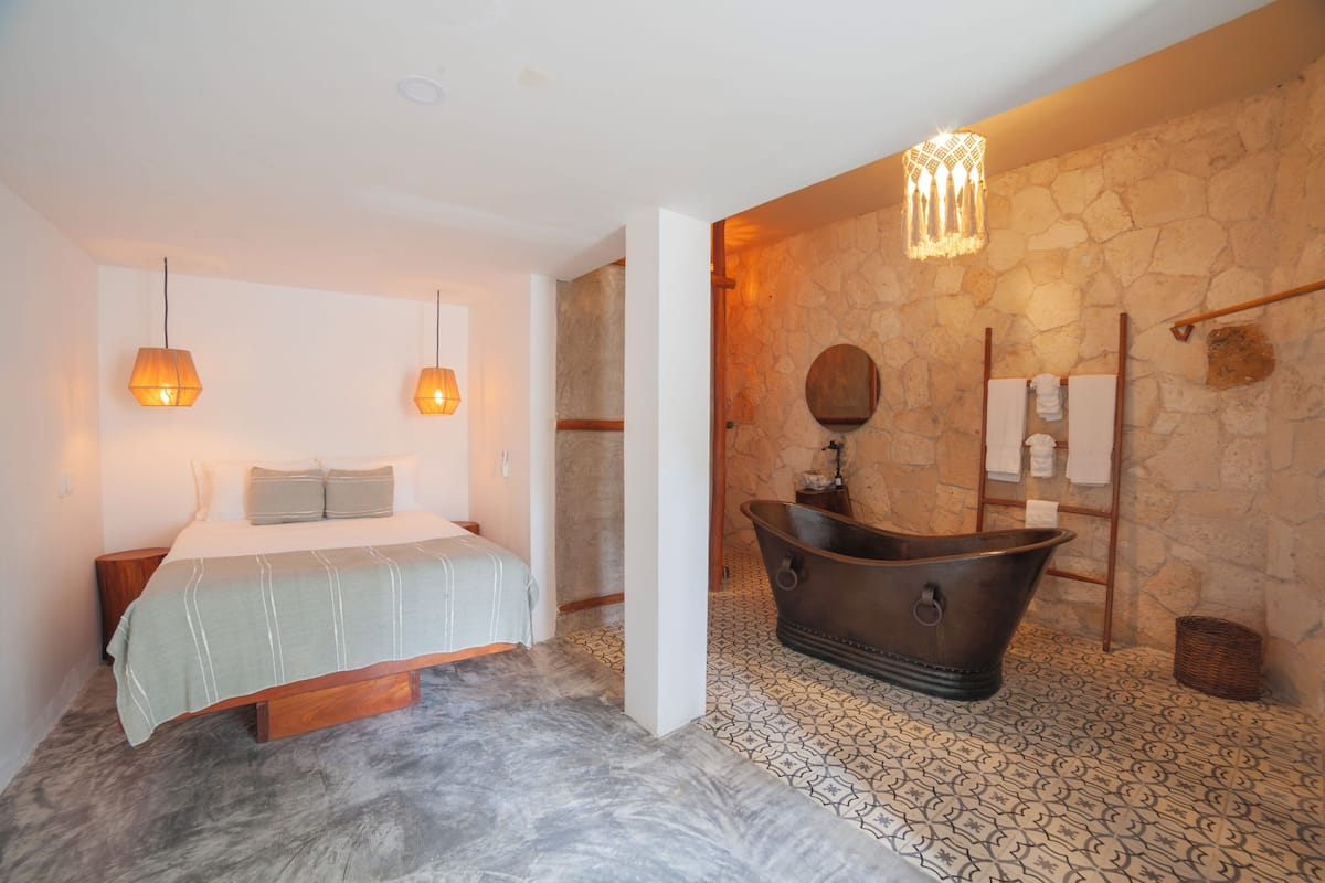 Un dormitorio con una cama, lámparas de noche, una pared de piedra, una bañera y una escalera de madera.