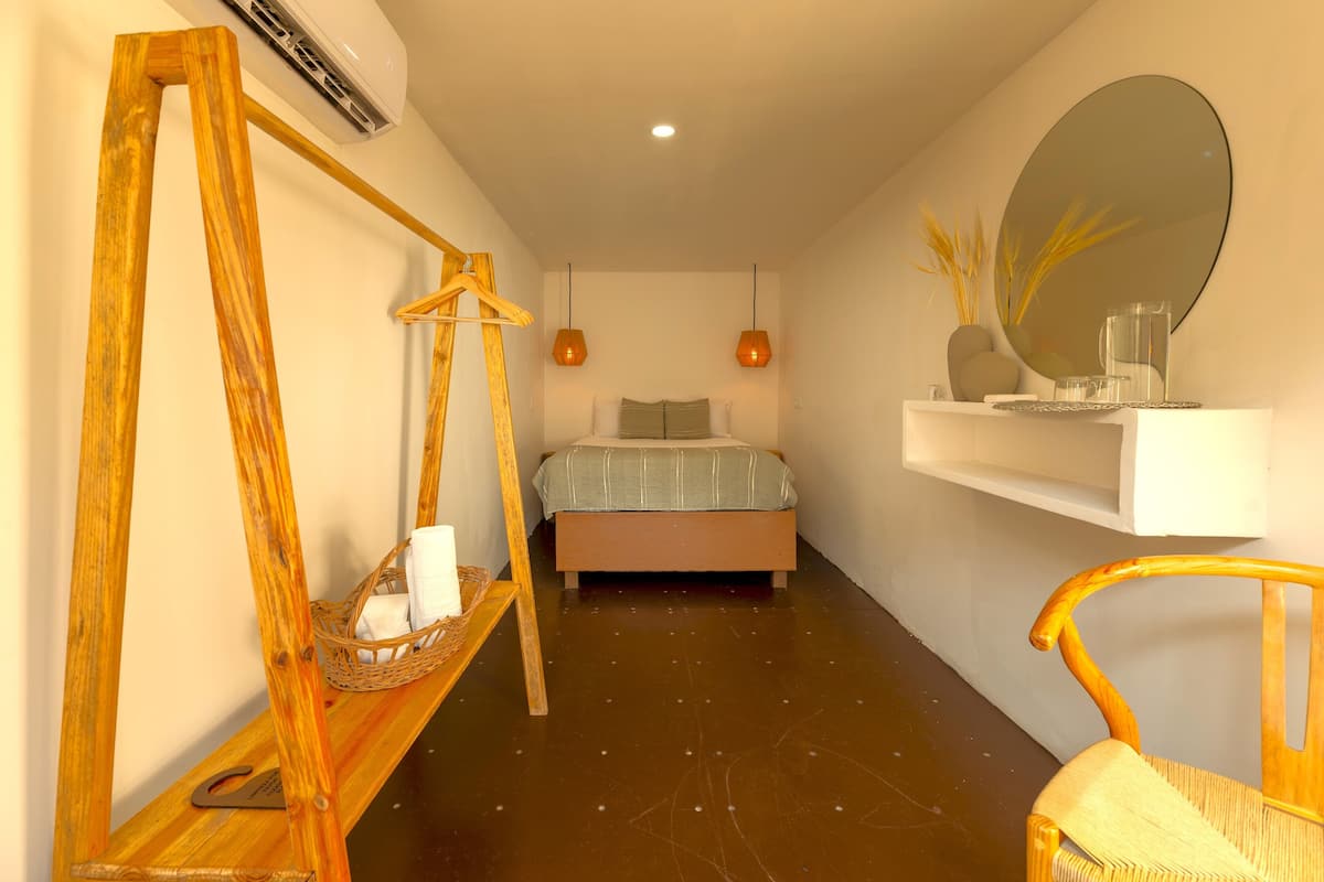 Un dormitorio con cama, una silla de madera, una mecedora, un estante con adornos y un espejo grande.