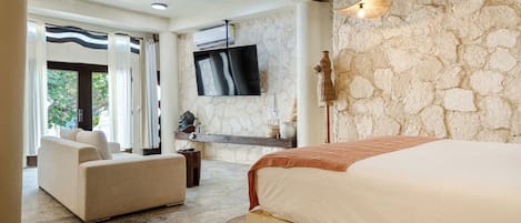 Un dormitorio moderno con una cama grande, un sofá, un televisor de pantalla plana y una pared de piedra.