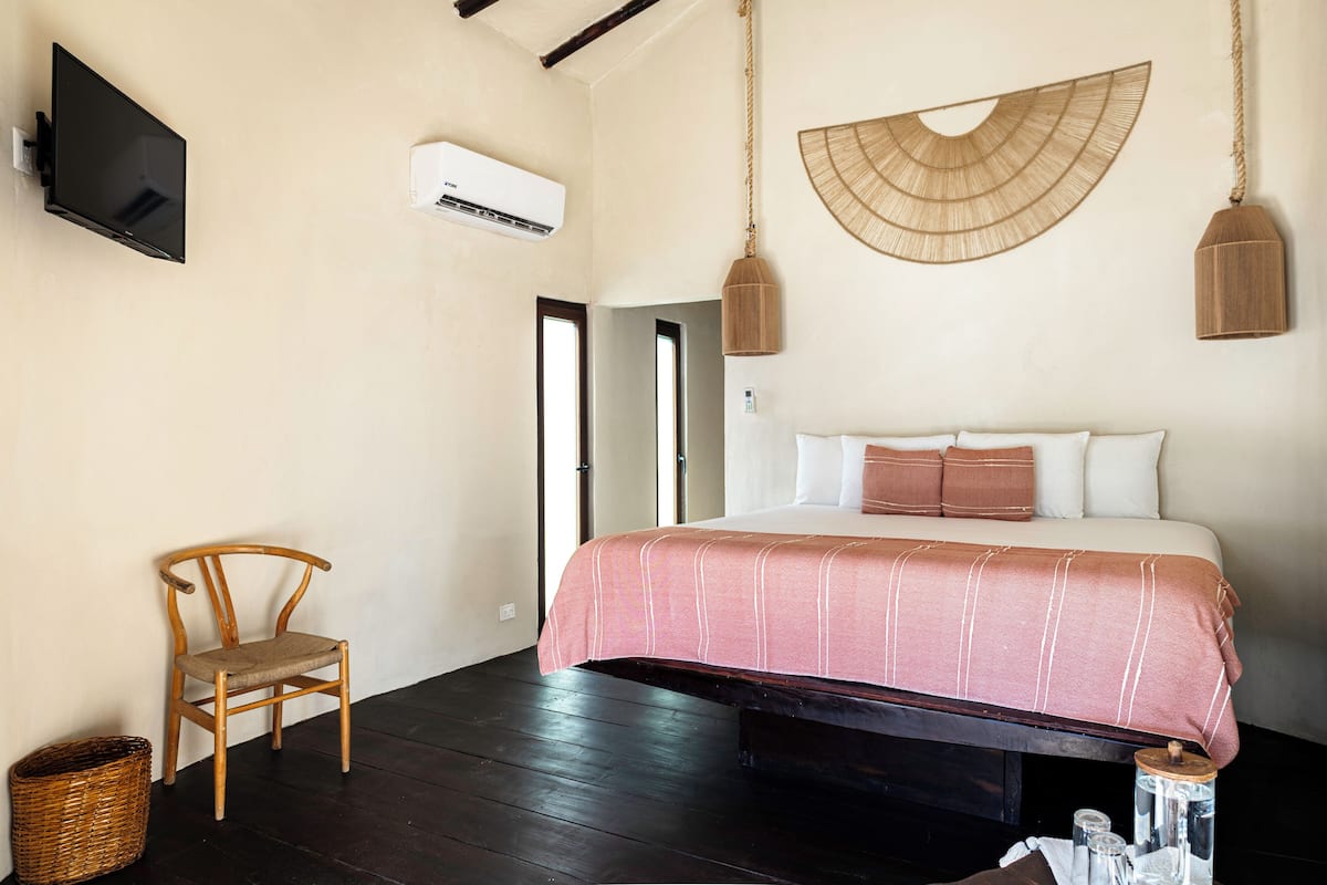 Un dormitorio con una cama, una silla, un televisor y una lámpara colgante.
