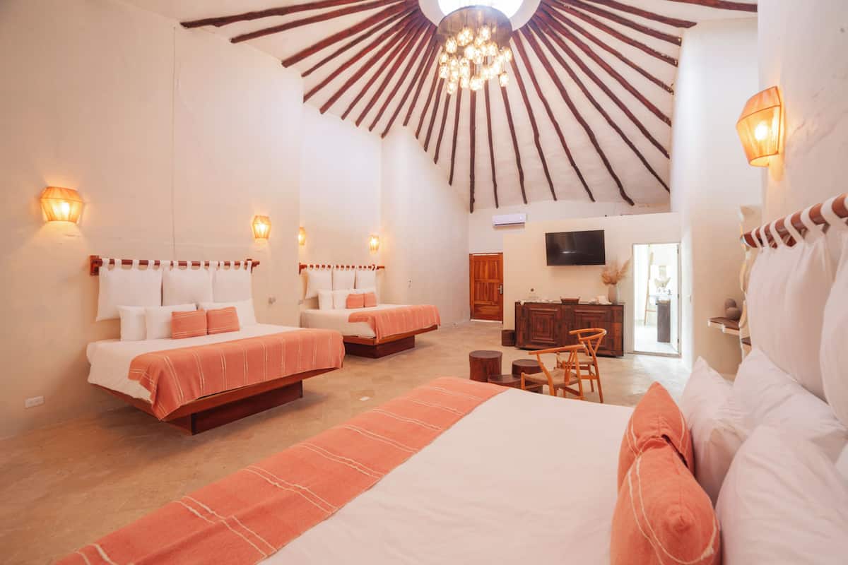 Un dormitorio amplio con dos camas, techo de madera y televisor en la pared.
