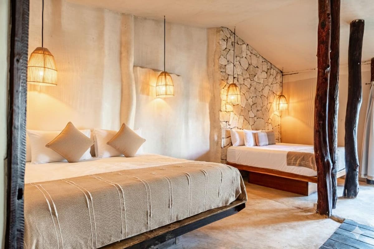 Un dormitorio con dos camas, una pared de piedra y lámparas colgantes.