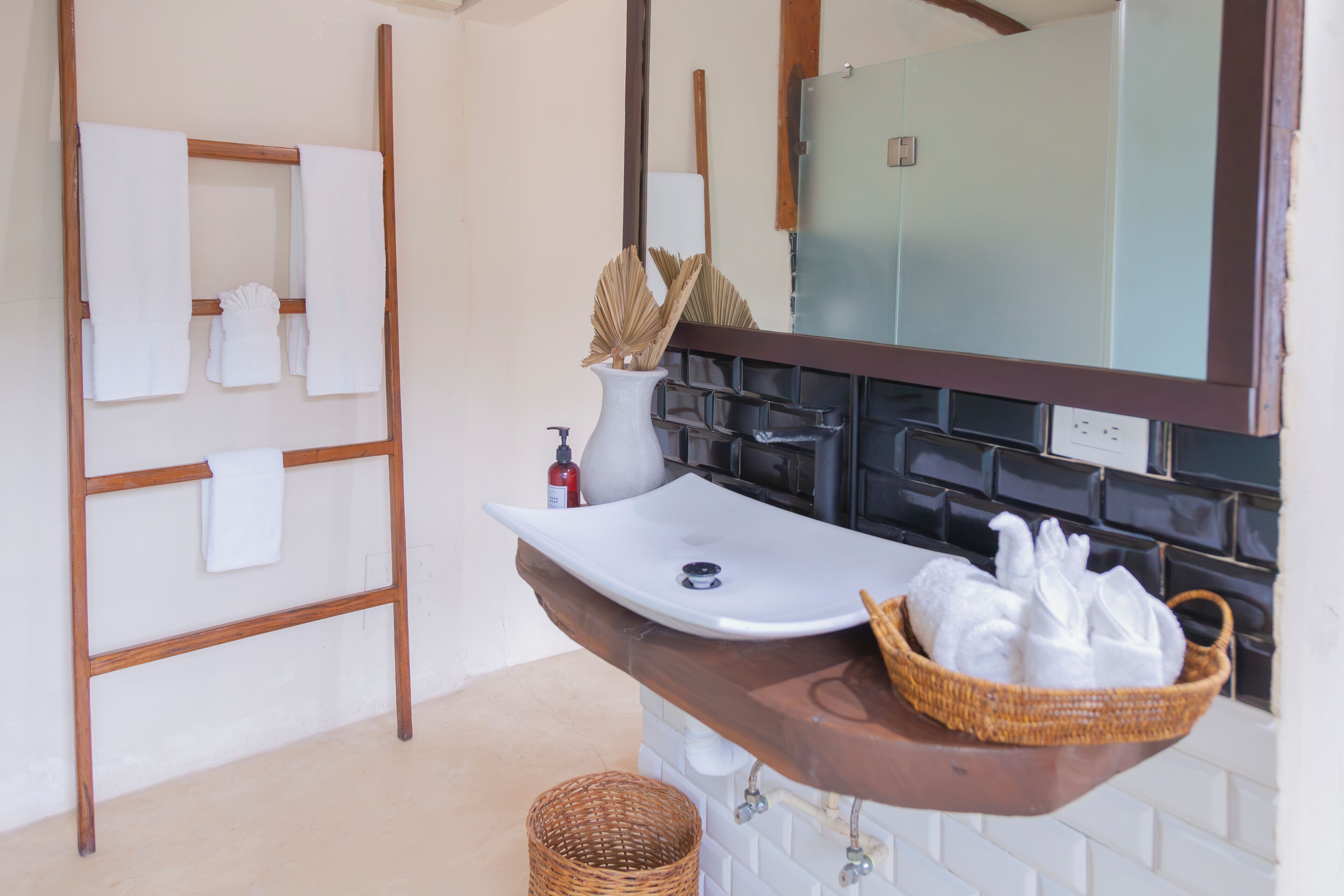 Une salle de bain avec un porte-serviettes en bois, un lavabo blanc, un miroir et un panier en osier contenant des serviettes.
