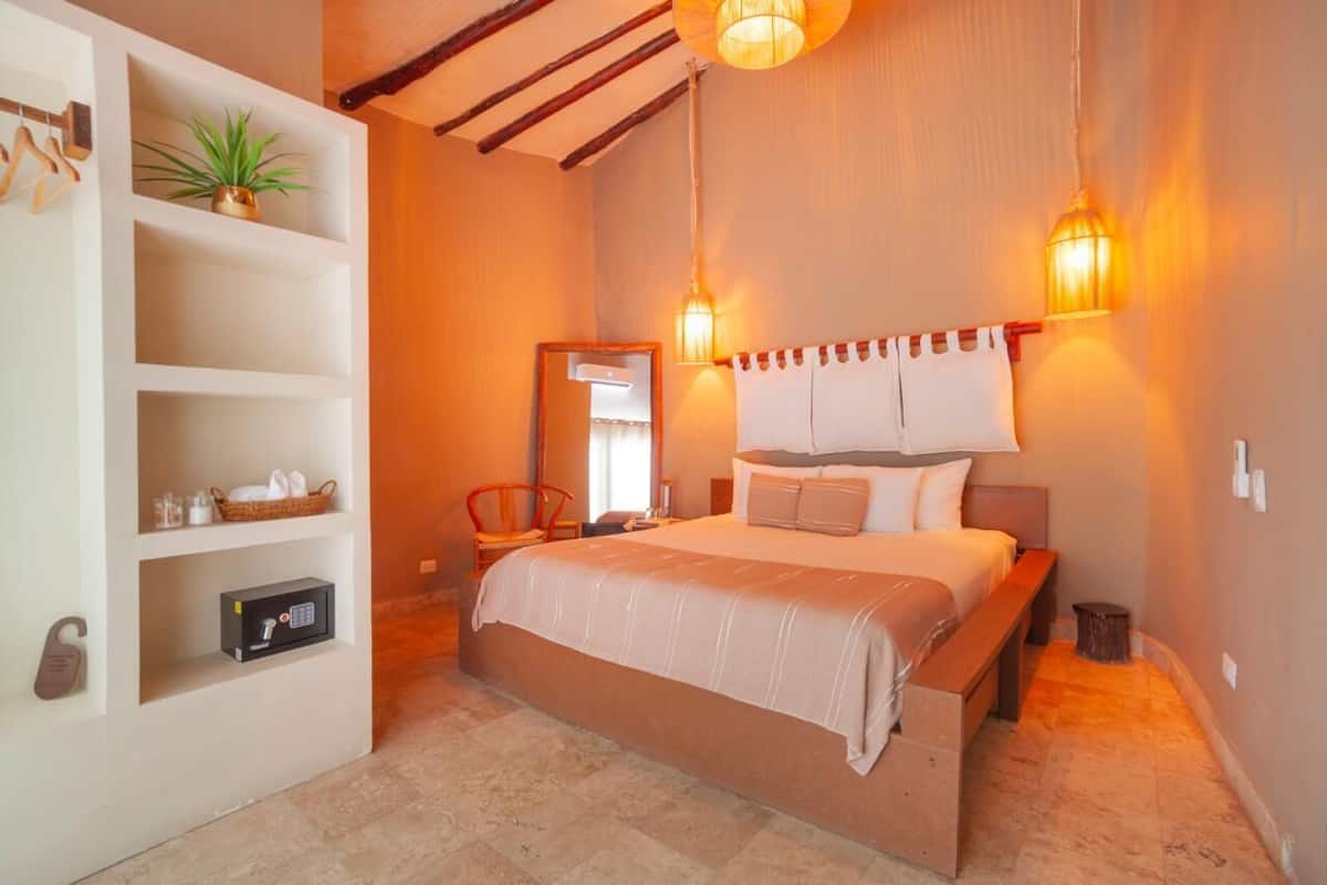 Un dormitorio con cama, lámparas de noche, una estantería con una planta, un espejo y una mesita de noche.