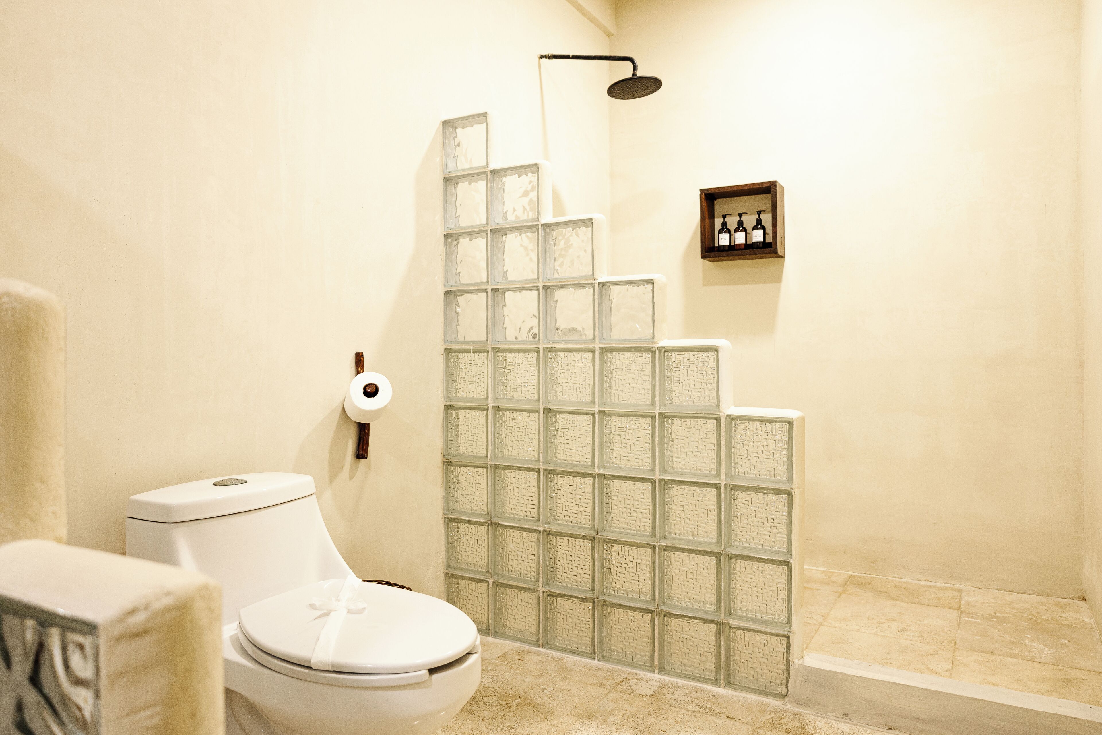 Un baño con inodoro, cabina de ducha de vidrio y un estante con artículos de aseo.