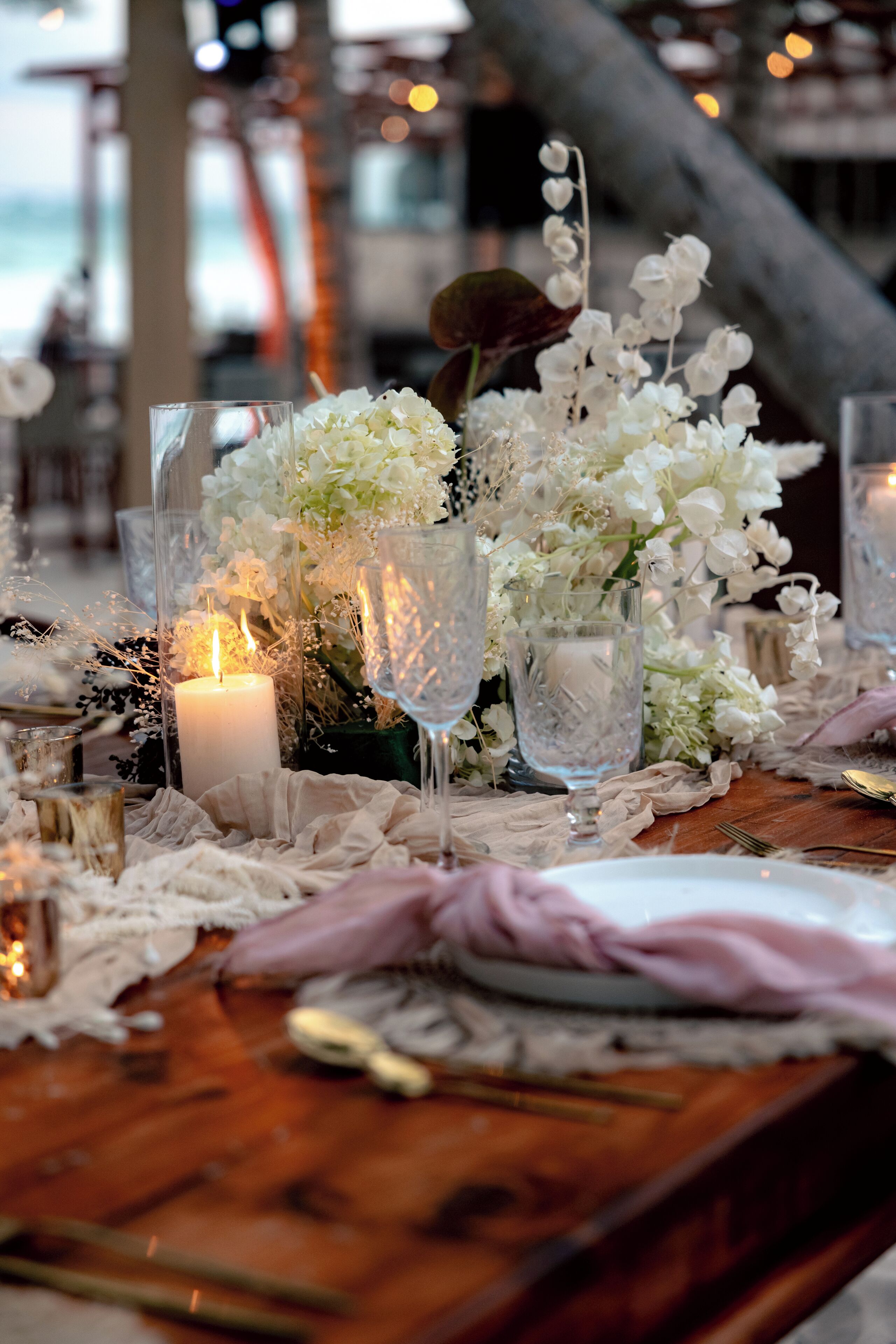 A table set with white flowers, candles, and glassware, suggesting a formal dining setting.