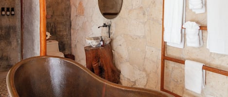Un baño con pared de piedra, una bañera de madera, un lavabo de madera y un perchero con varias toallas.