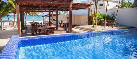 A poolside area with a wooden pergola, outdoor seating, and a view of the ocean.
