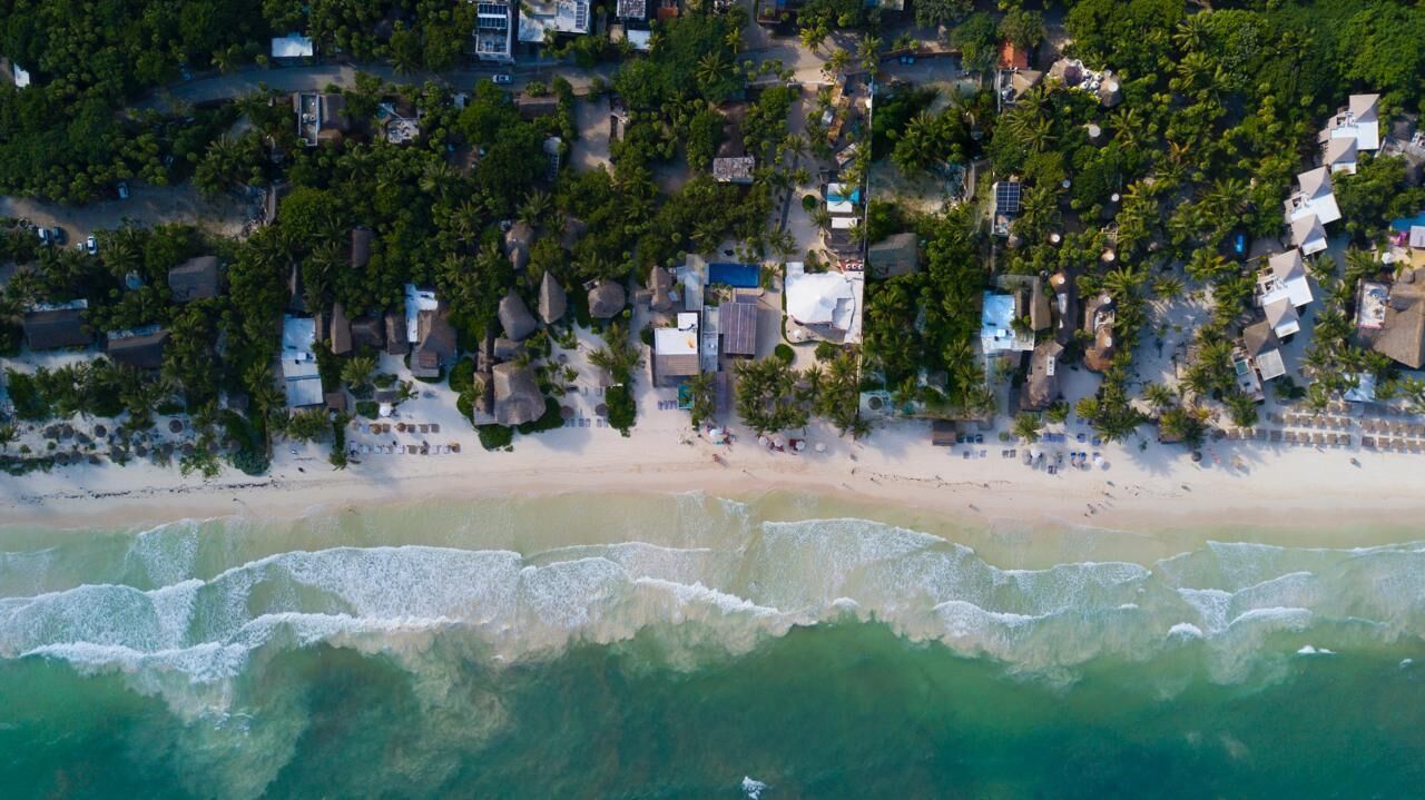 Vista aérea de una zona residencial costera con casas, playa y olas del océano.