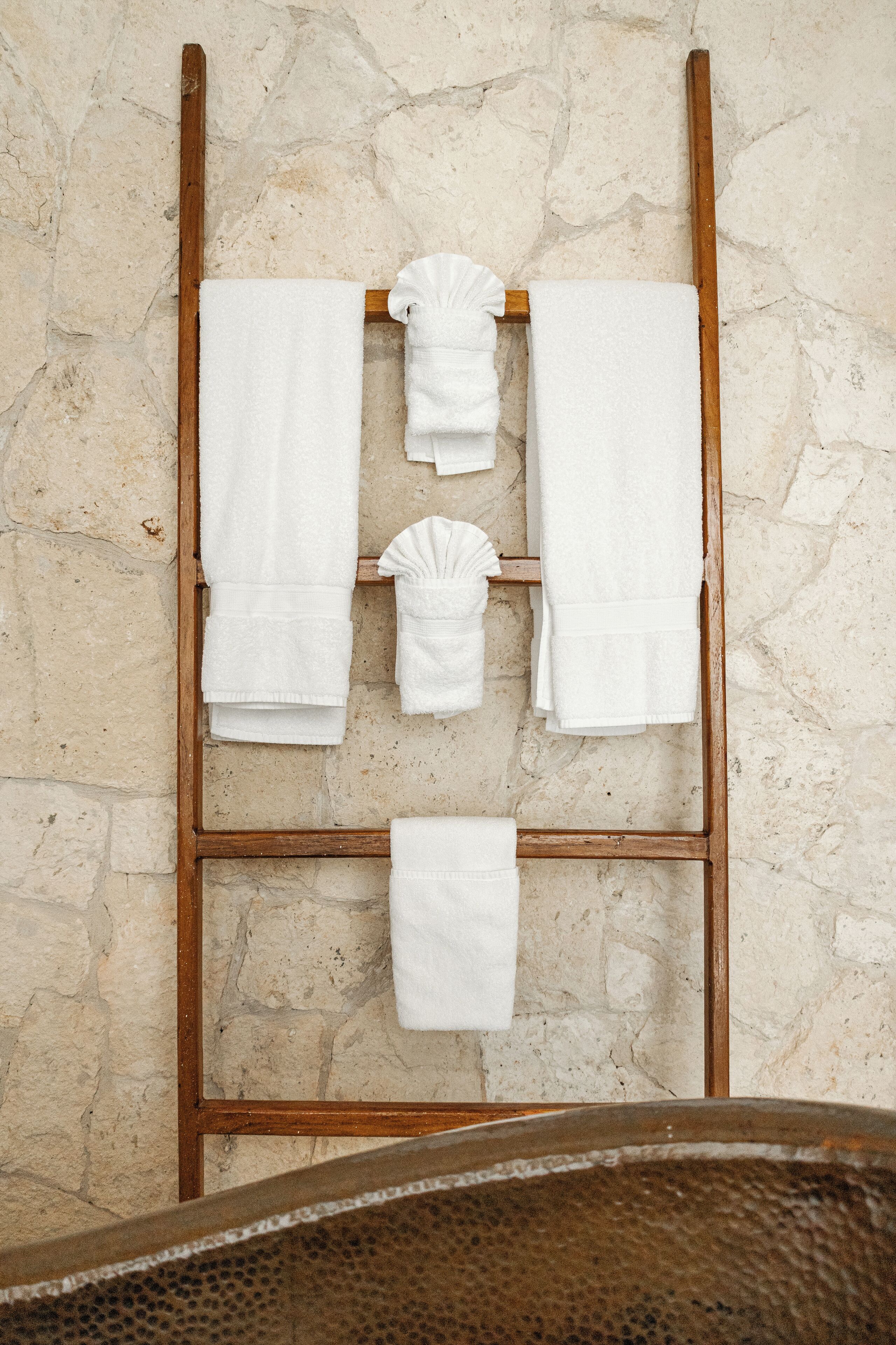 A wooden towel rack with four white towels hanging against a textured stone wall.