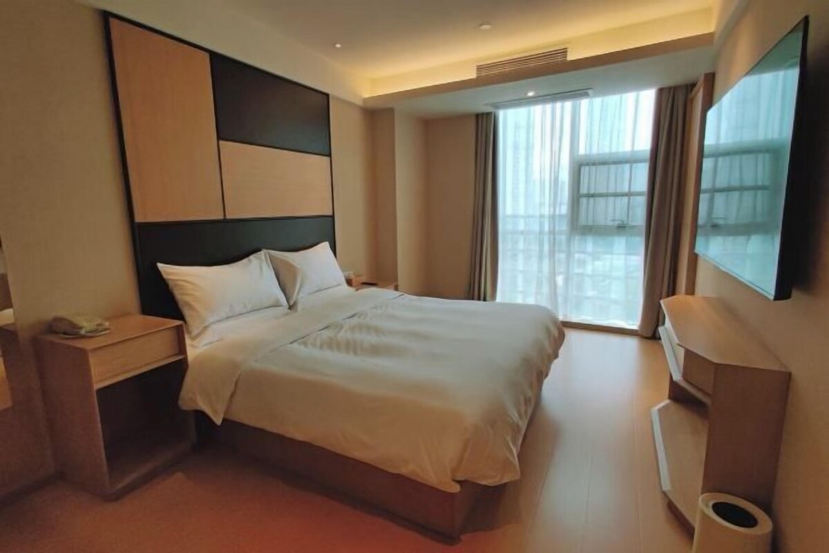 A hotel room with a large bed, a bedside table, a TV, and a window with curtains.