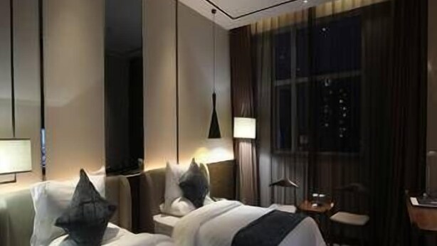 Habitación de hotel con dos camas, un escritorio, una silla y un ventanal con cortinas.
