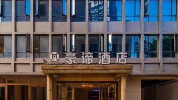 A hotel facade with a grid of windows and a central entrance with a sign.