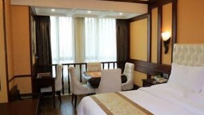 A hotel room with a large bed, a desk with a chair, a small table, and a window with curtains.