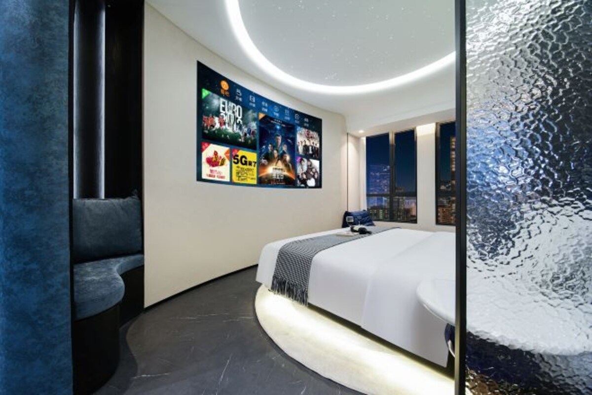 A modern bedroom with a curved bed, a city view, and a wall with promotional posters.