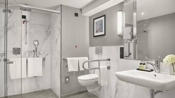 A modern bathroom with a glass-enclosed shower, a white toilet, and a large sink with a mirror.