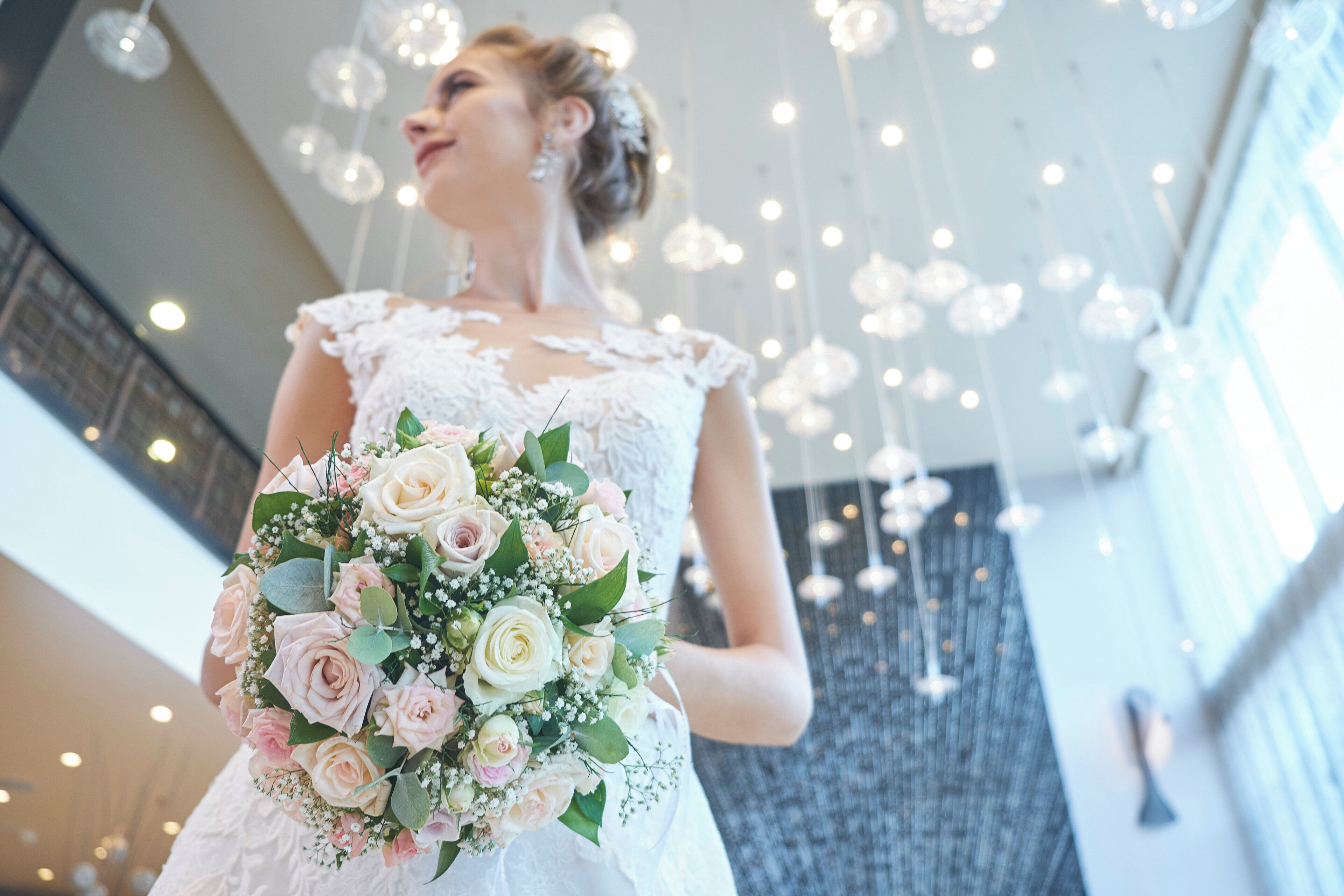A person holding a bouquet of flowers in a room with hanging lights and a patterned wall.