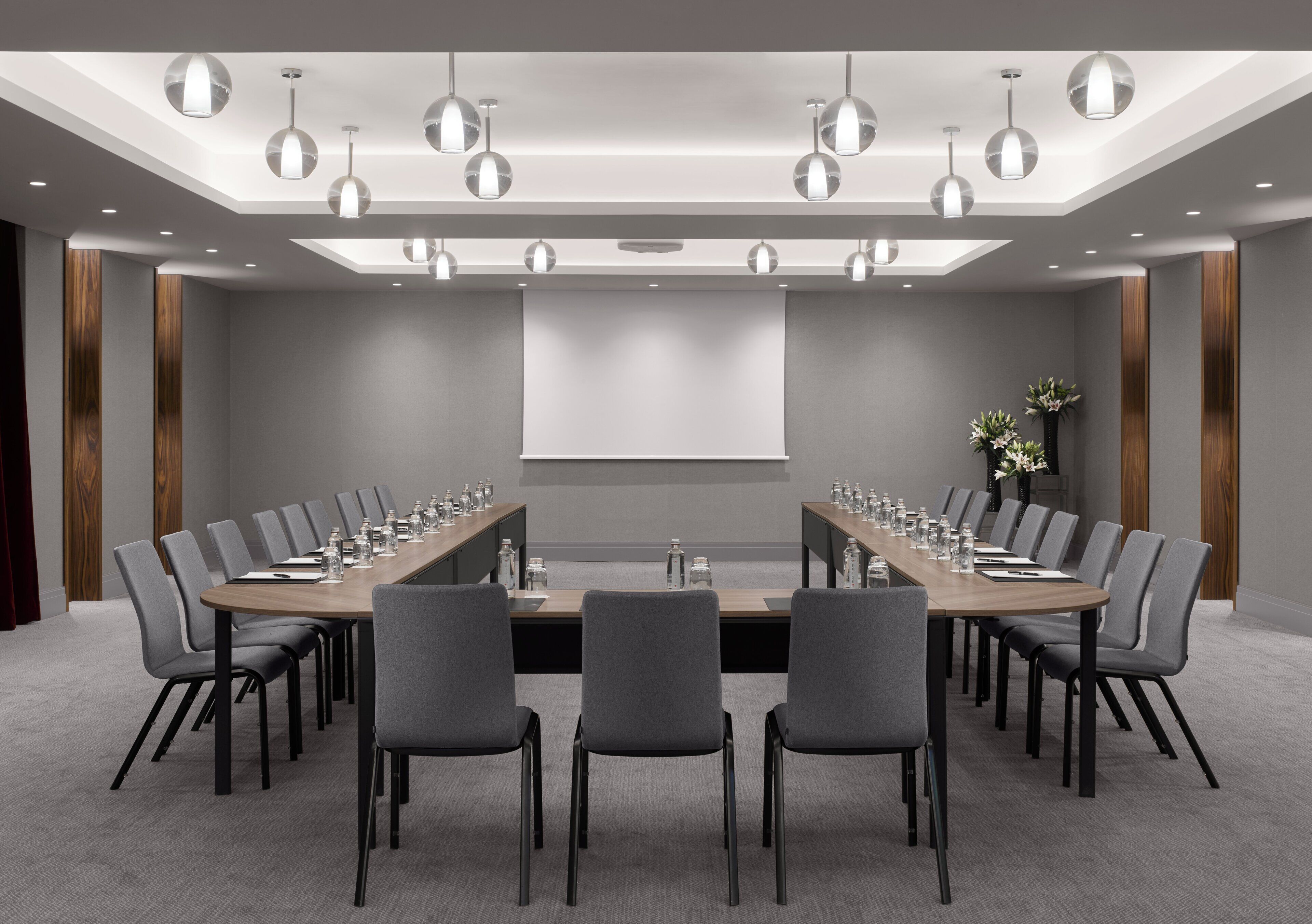 Une salle de conférence équipée d’une longue table, de nombreuses chaises, d’un écran de projection et de luminaires suspendus.