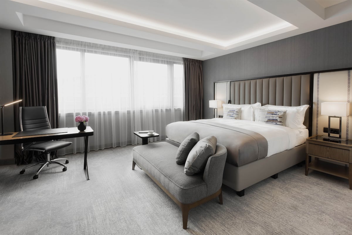 A modern hotel room with a large bed, a desk, a chair, and a small table.