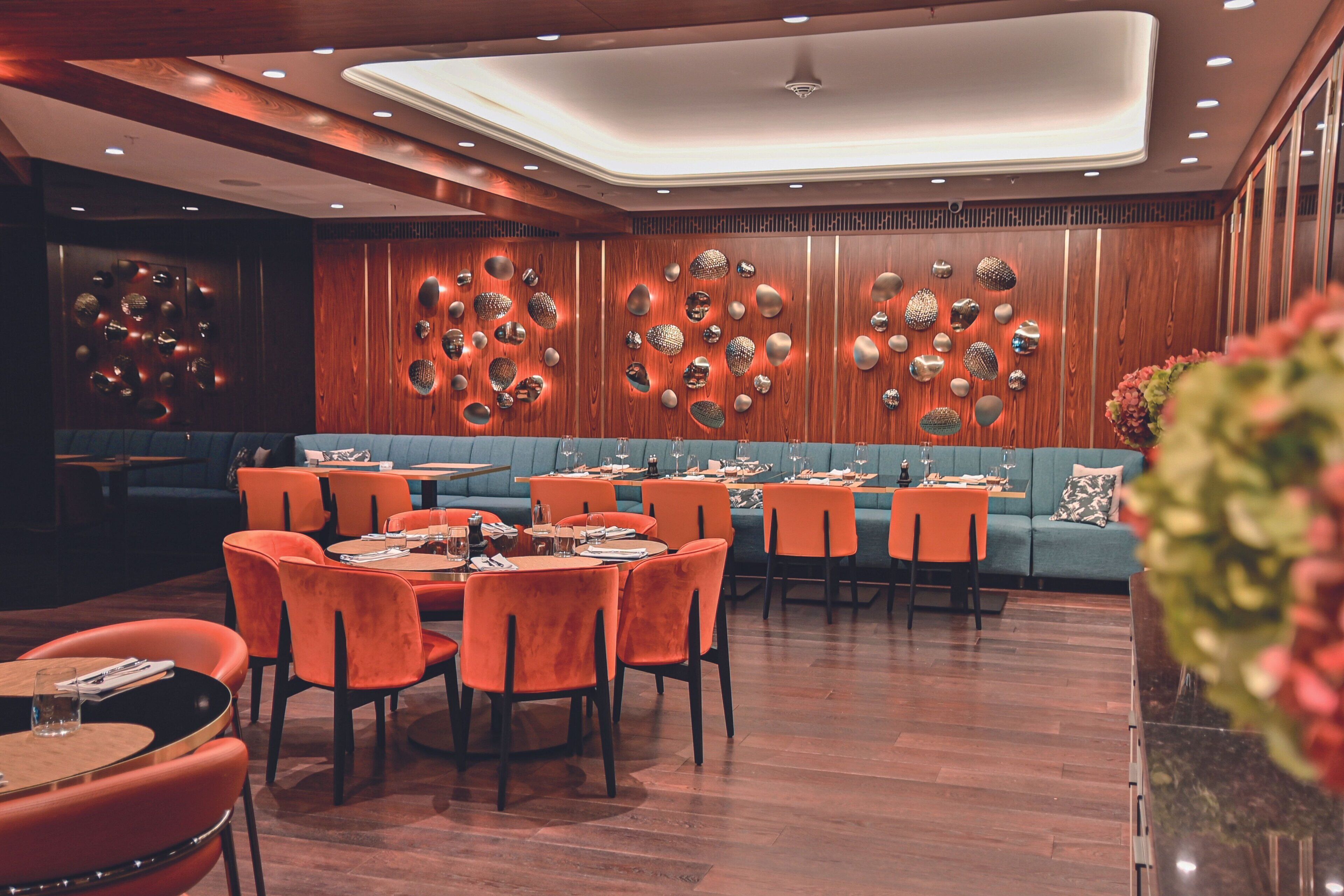 A restaurant with wooden panel walls, orange chairs, and tables set for dining.
