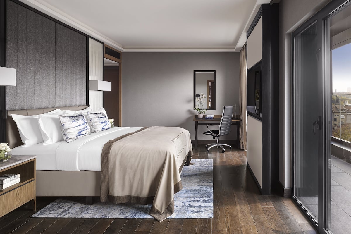 A modern hotel room with a large bed, a desk, and a view of the city through the window.