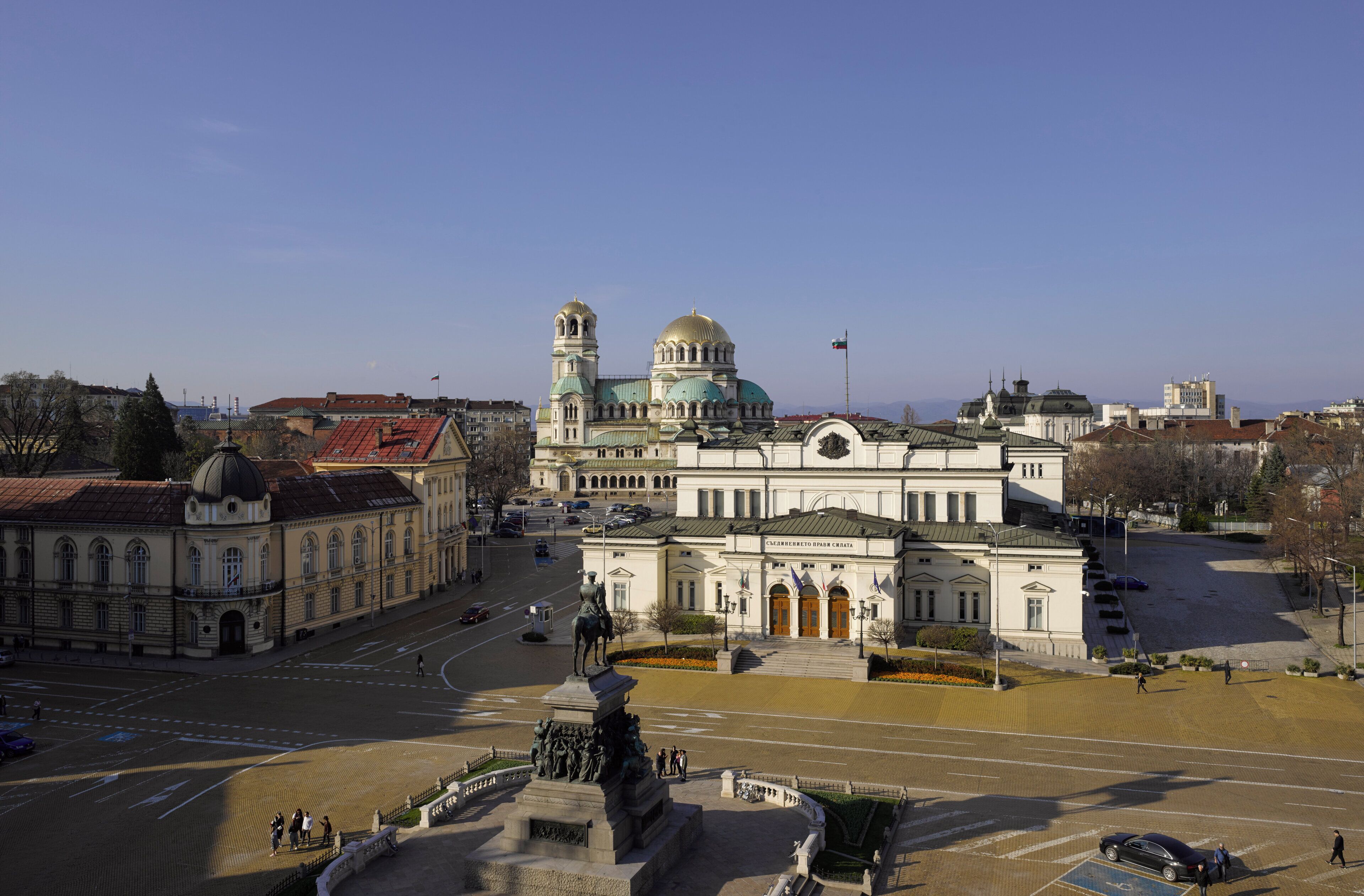 A large public square with a prominent building featuring a dome and a statue in the center.