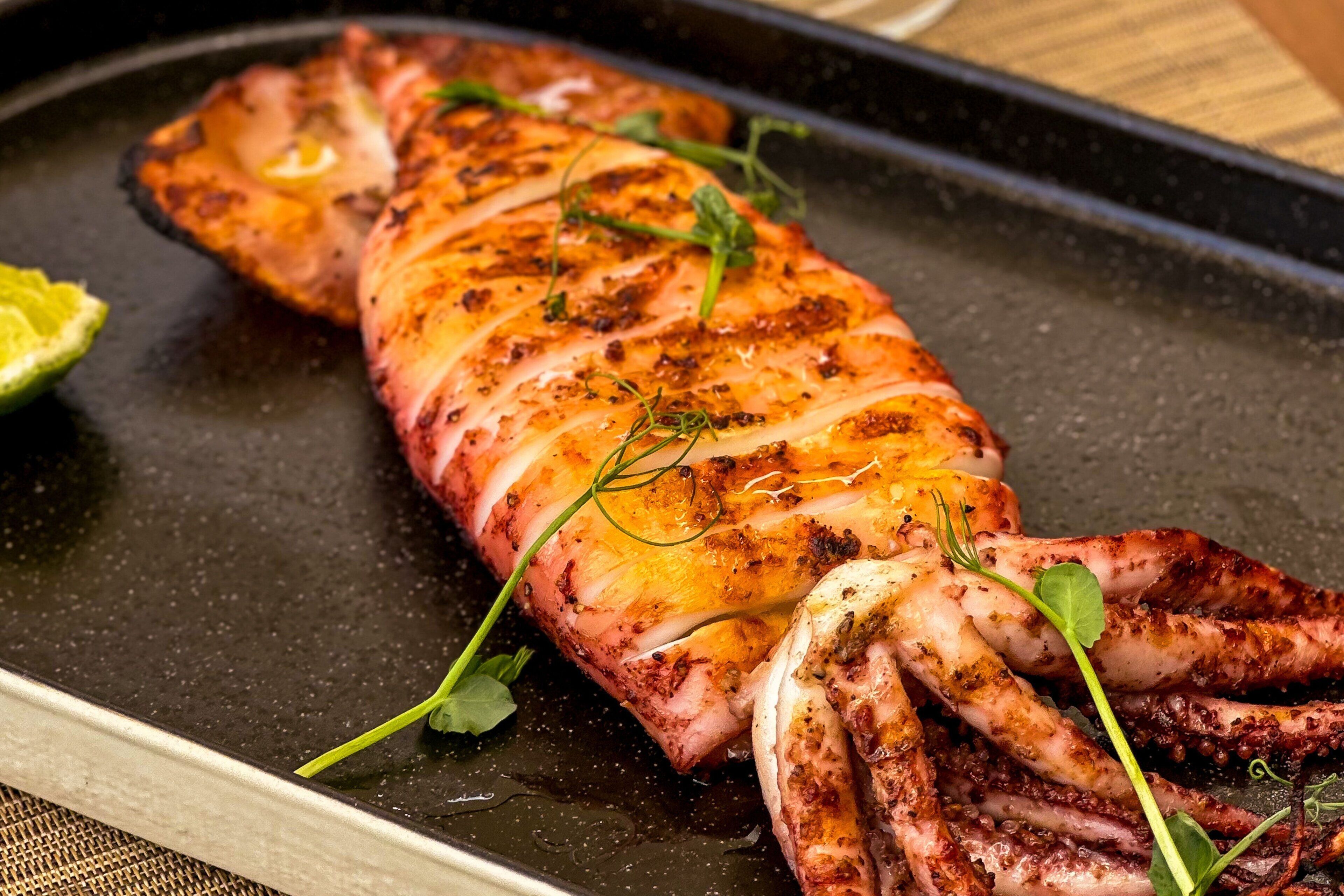 Plato con pulpo a la parrilla, hierbas y presentación elegante.