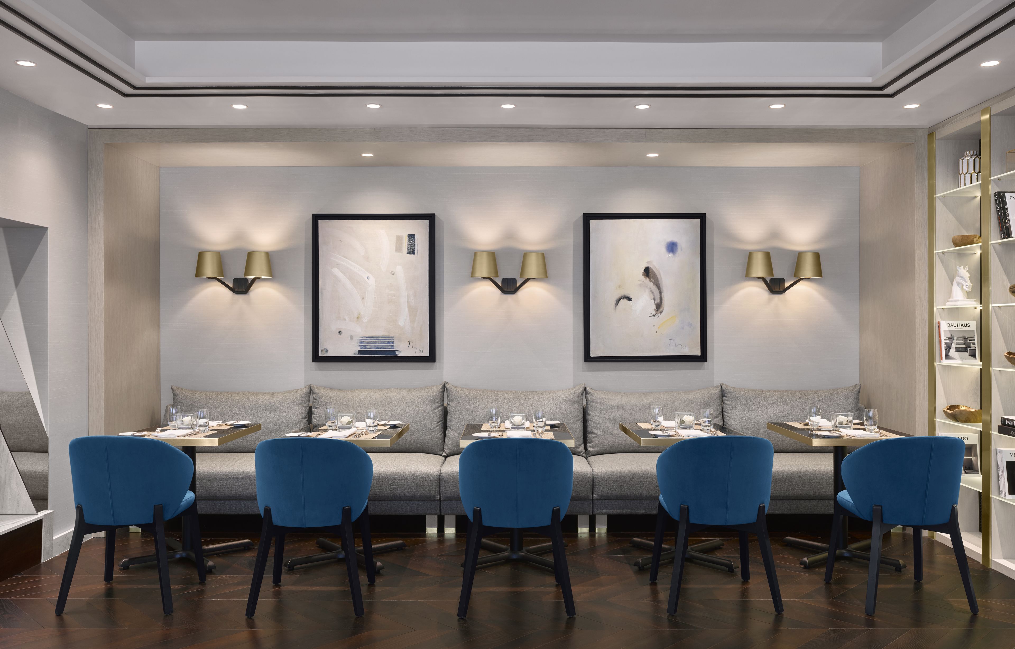 A modern hotel lobby with a sofa, four blue chairs, and two wall-mounted lamps.