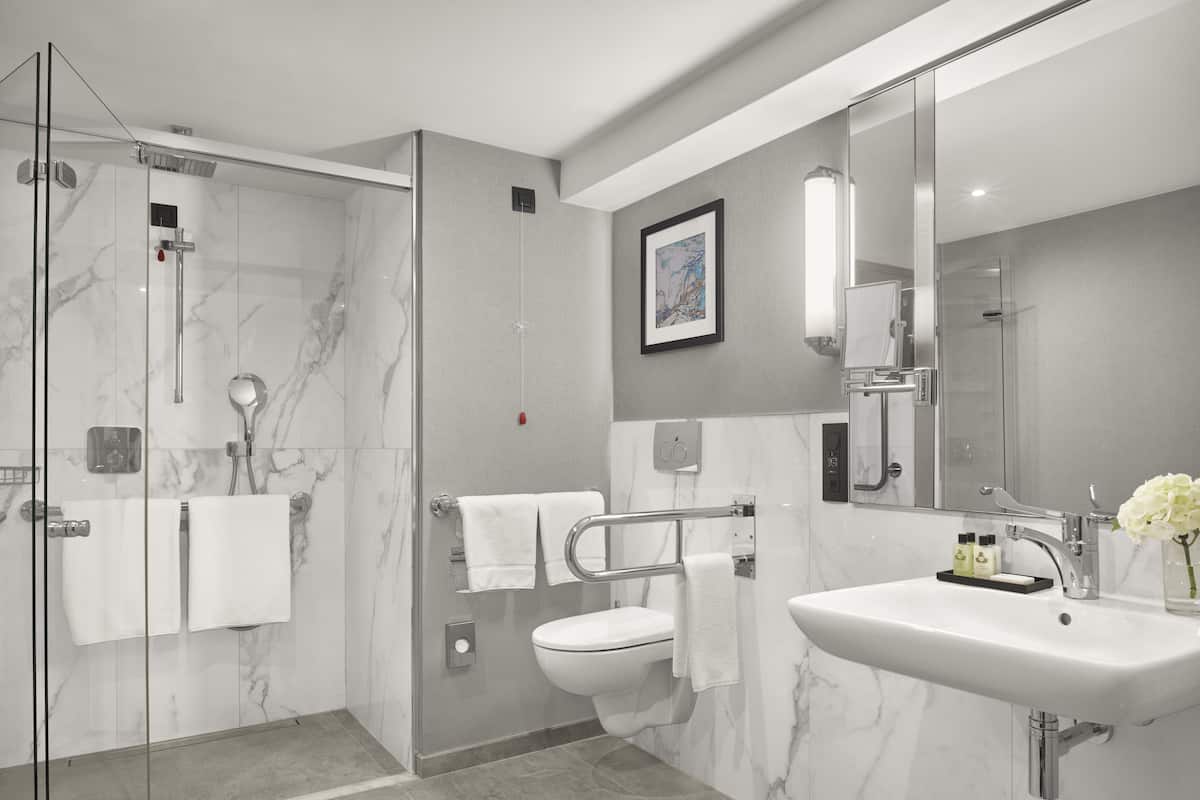 A modern bathroom with a glass-enclosed shower, a toilet, and a sink with a mirror.