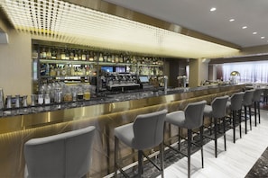A bar area with a long counter, bar stools, and a well-stocked shelf of liquor bottles.