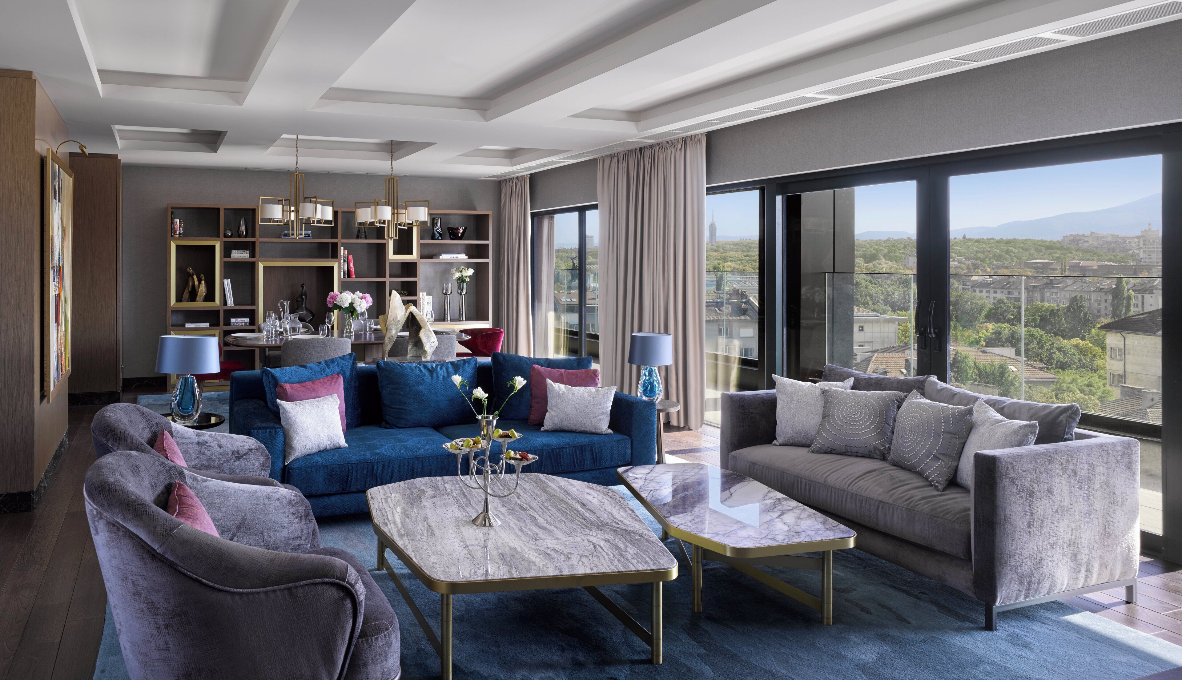 Un salon moderne avec un canapé bleu, des fauteuils gris et une table basse en marbre.
