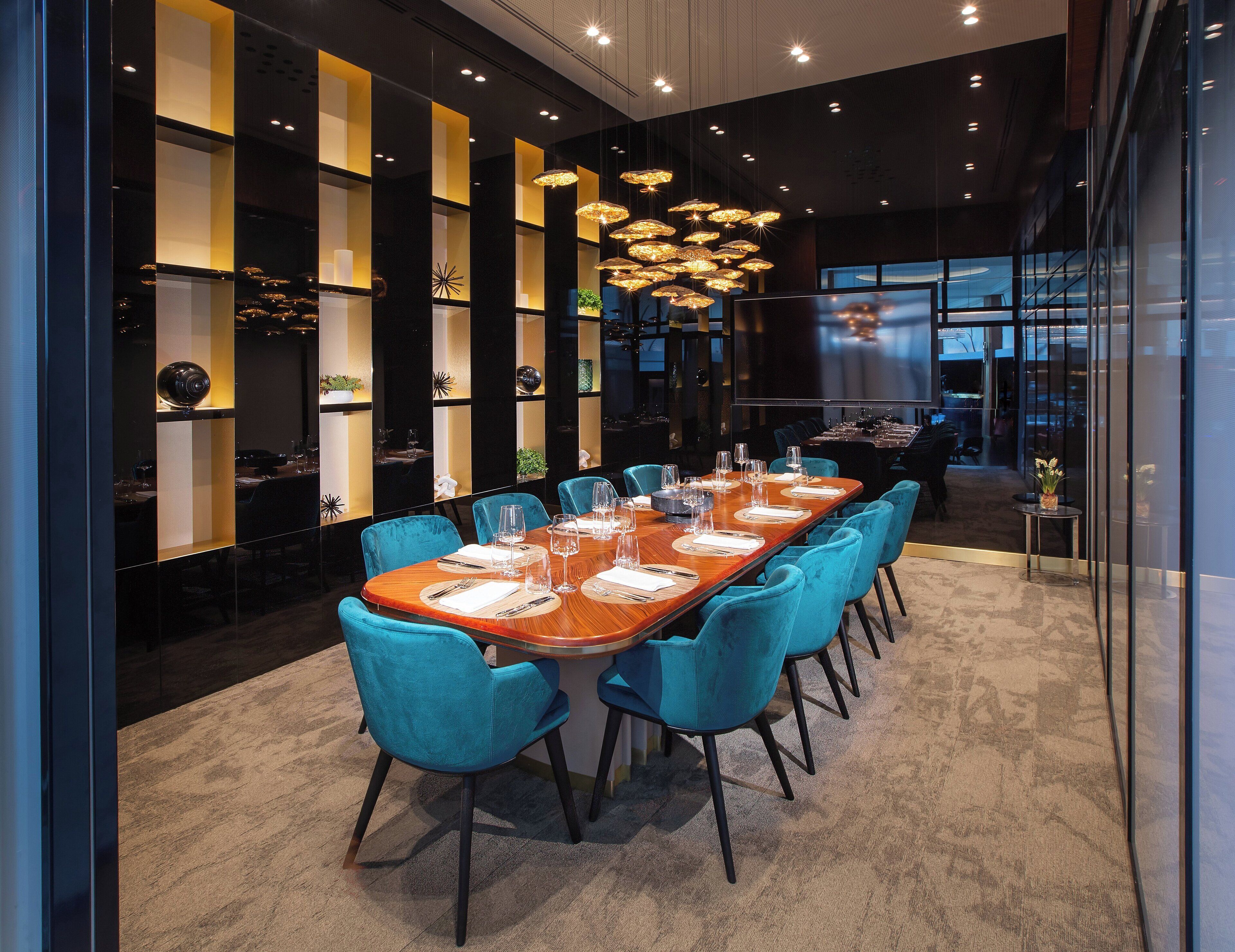 A modern dining area with a long wooden table set for a meal, surrounded by teal chairs.