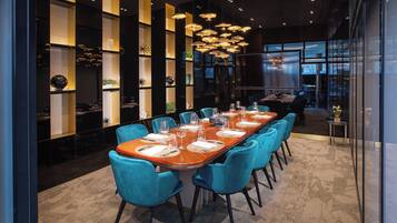 A modern dining area with a long wooden table set for a meal, surrounded by teal chairs.