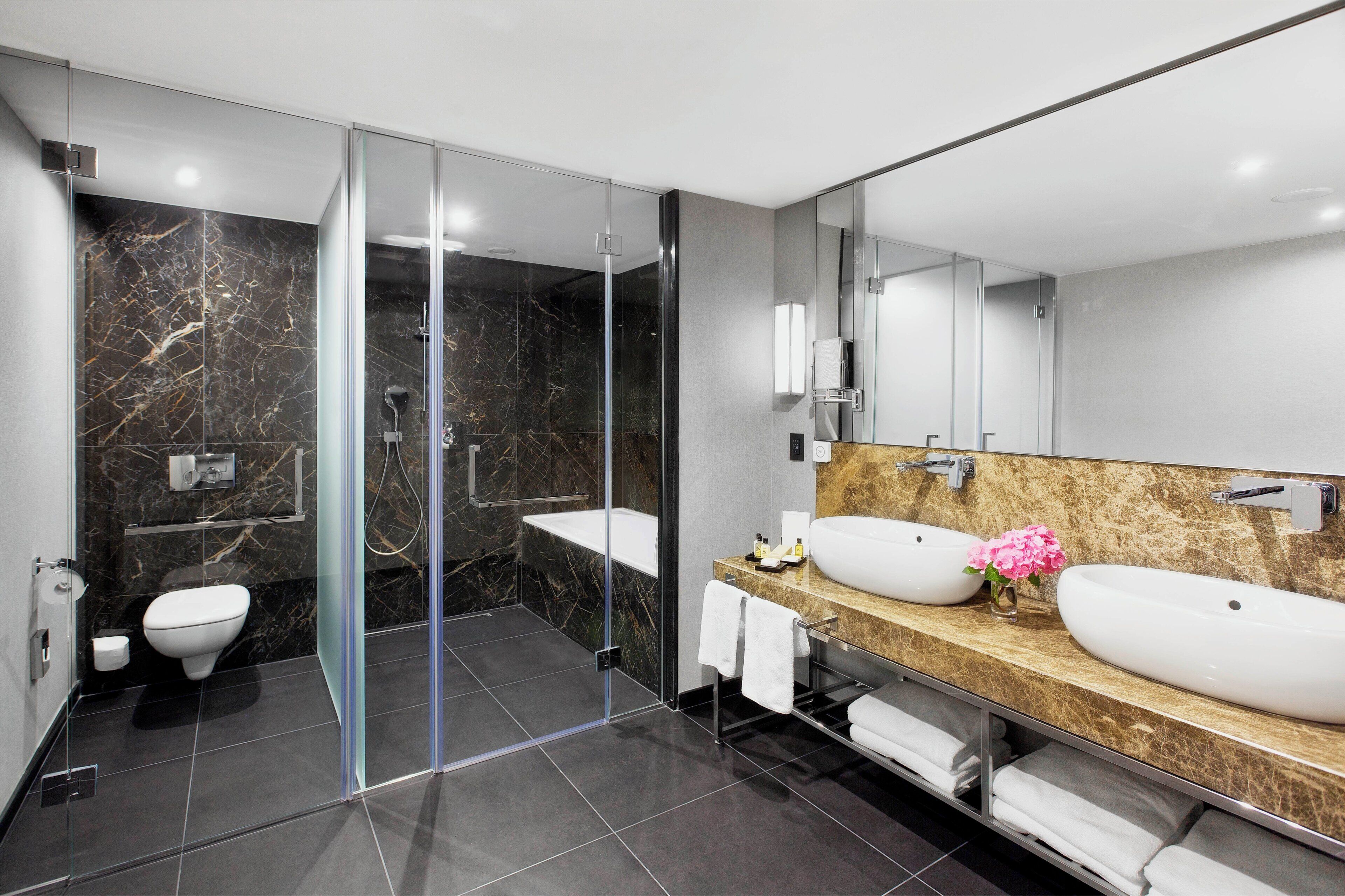 A modern bathroom with a glass-enclosed shower, a toilet, and two sinks with marble countertops.