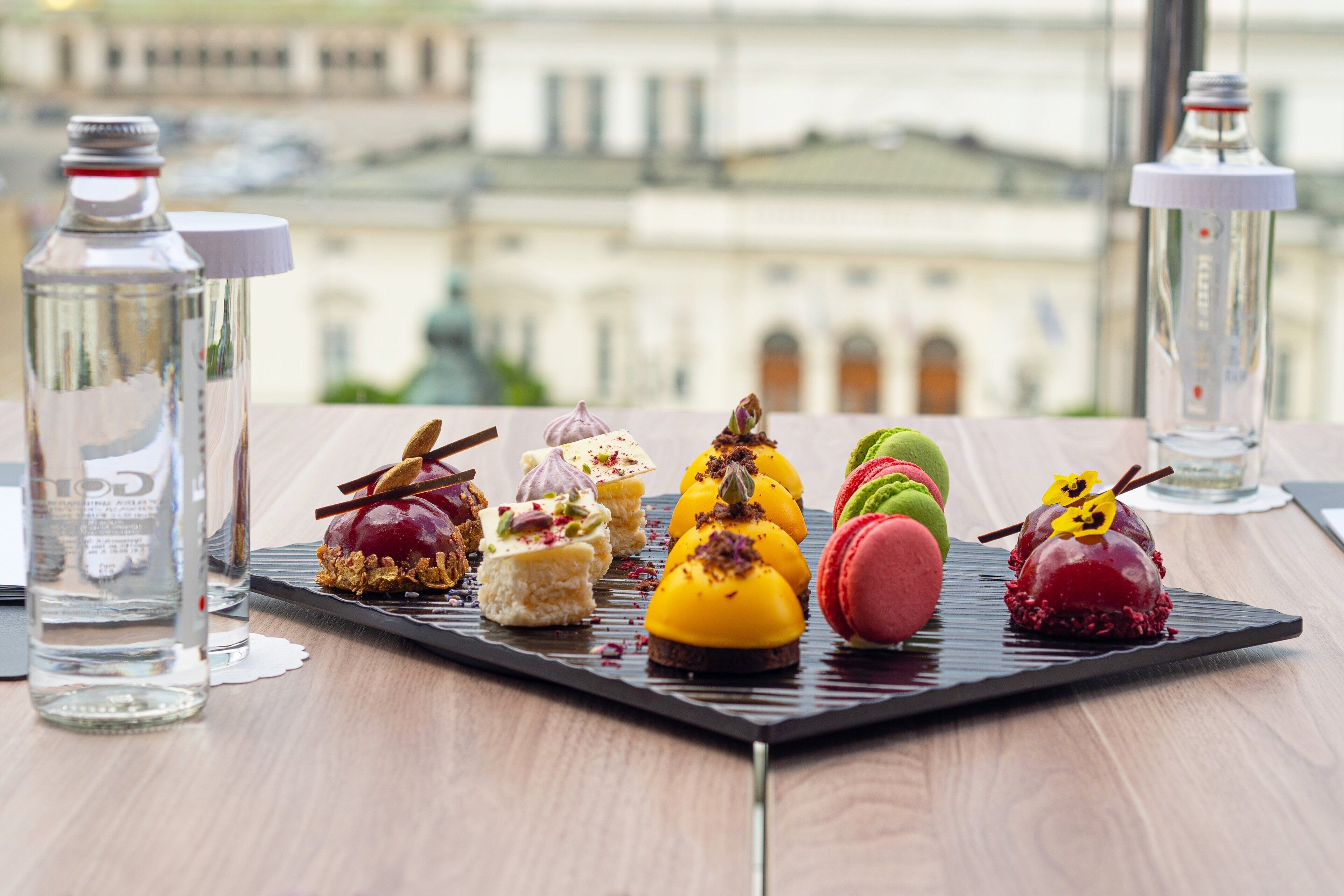 Variedad de postres sobre un plato negro, con vista a un paisaje urbano de fondo.