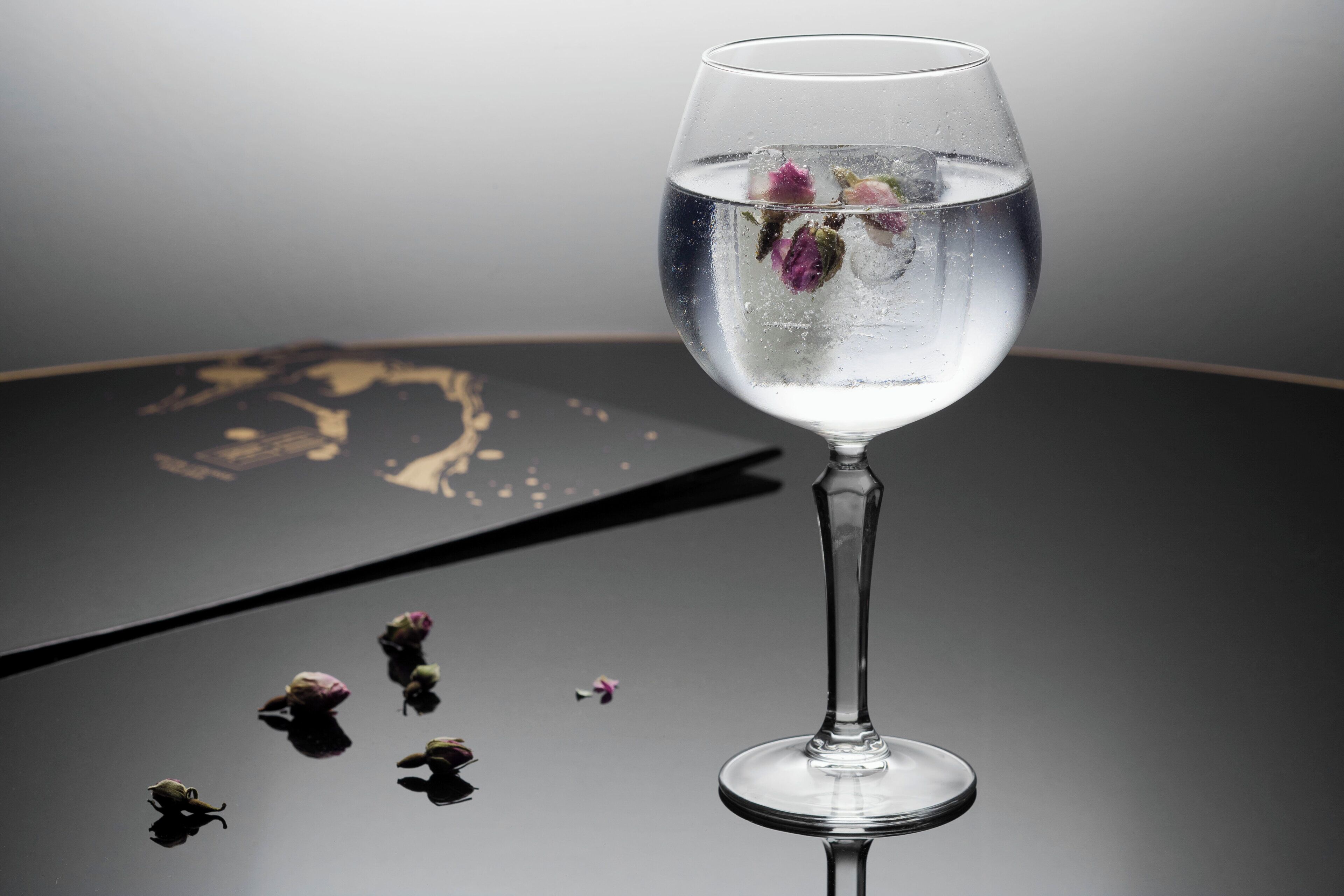 Un vaso transparente con agua y flores sobre una superficie reflectante.