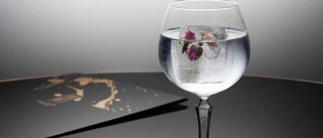 Un vaso transparente con agua y flores sobre una superficie reflectante.