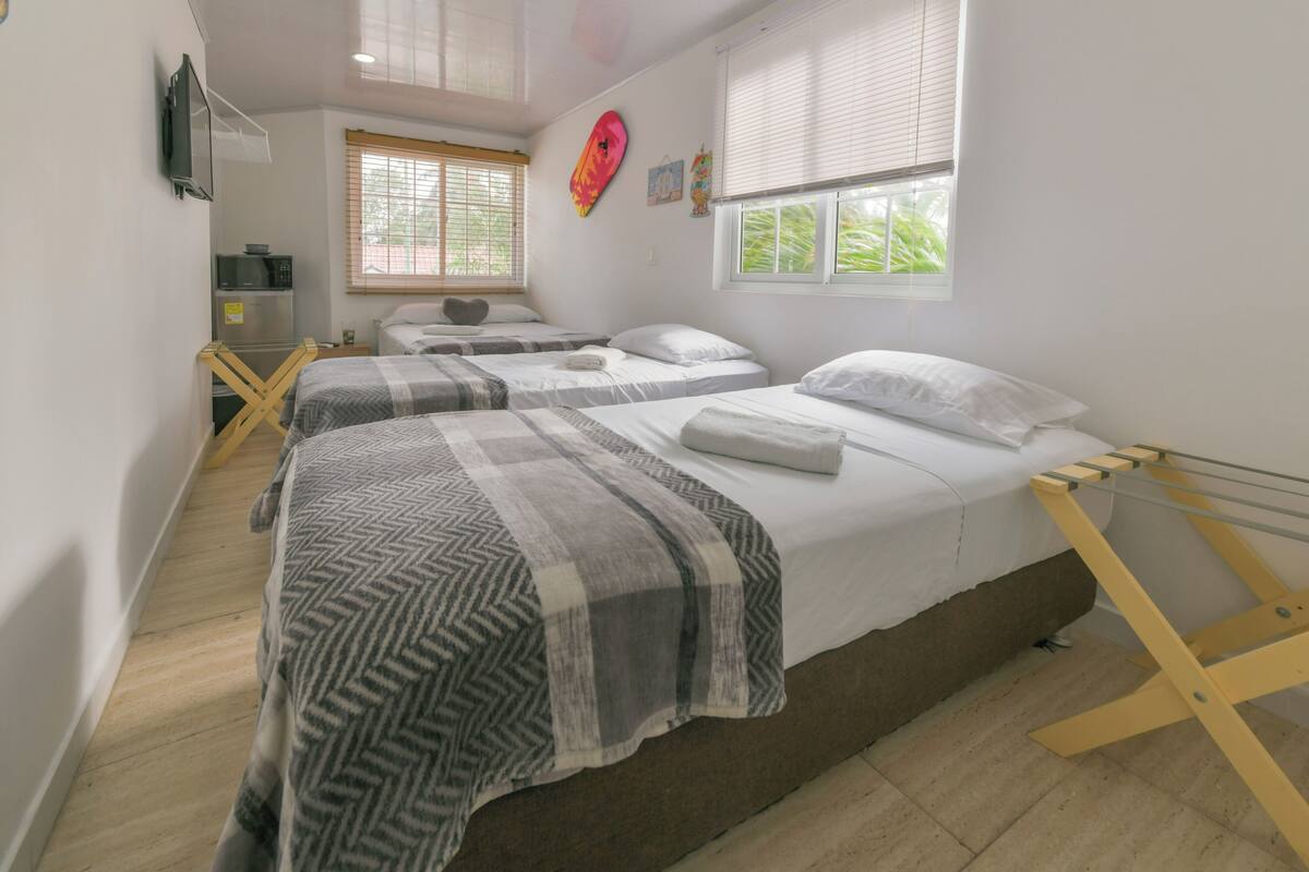 A room with two beds, a microwave, a small table, and a window with blinds.