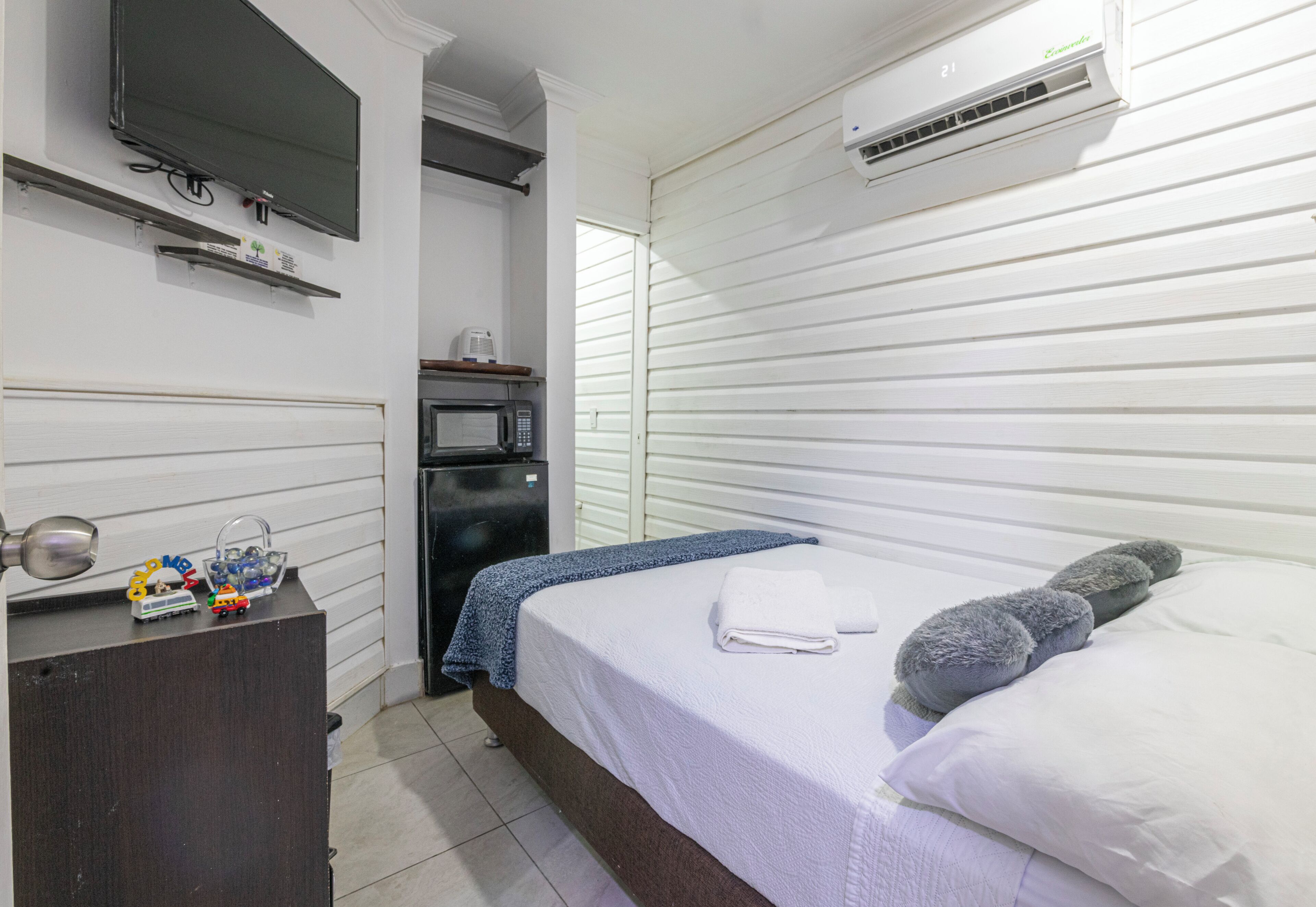 A bedroom with a bed, a TV, a microwave, and a dresser.