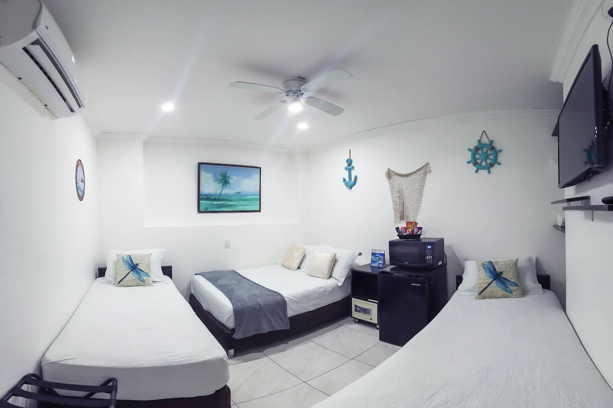 A hotel room with two single beds, a ceiling fan, an air conditioner, a television, and a small desk with a computer.